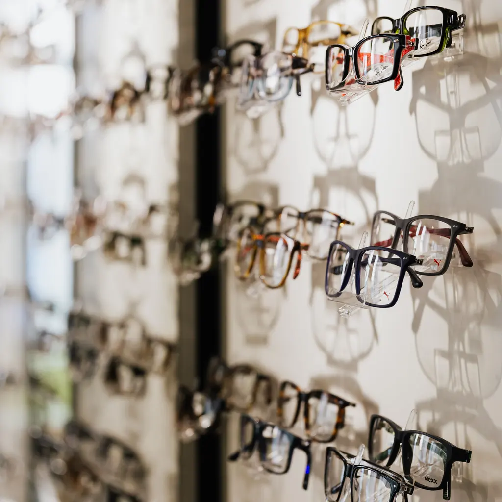 Eyeglass frames line wall-mounted display rails in an optical shop.