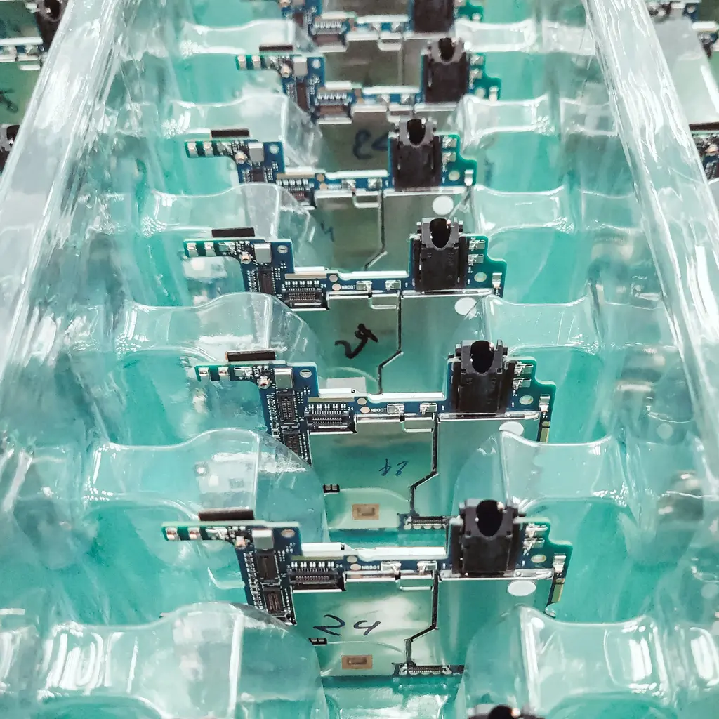 Rows of assembled circuit boards sit in shaped trays at a production station.