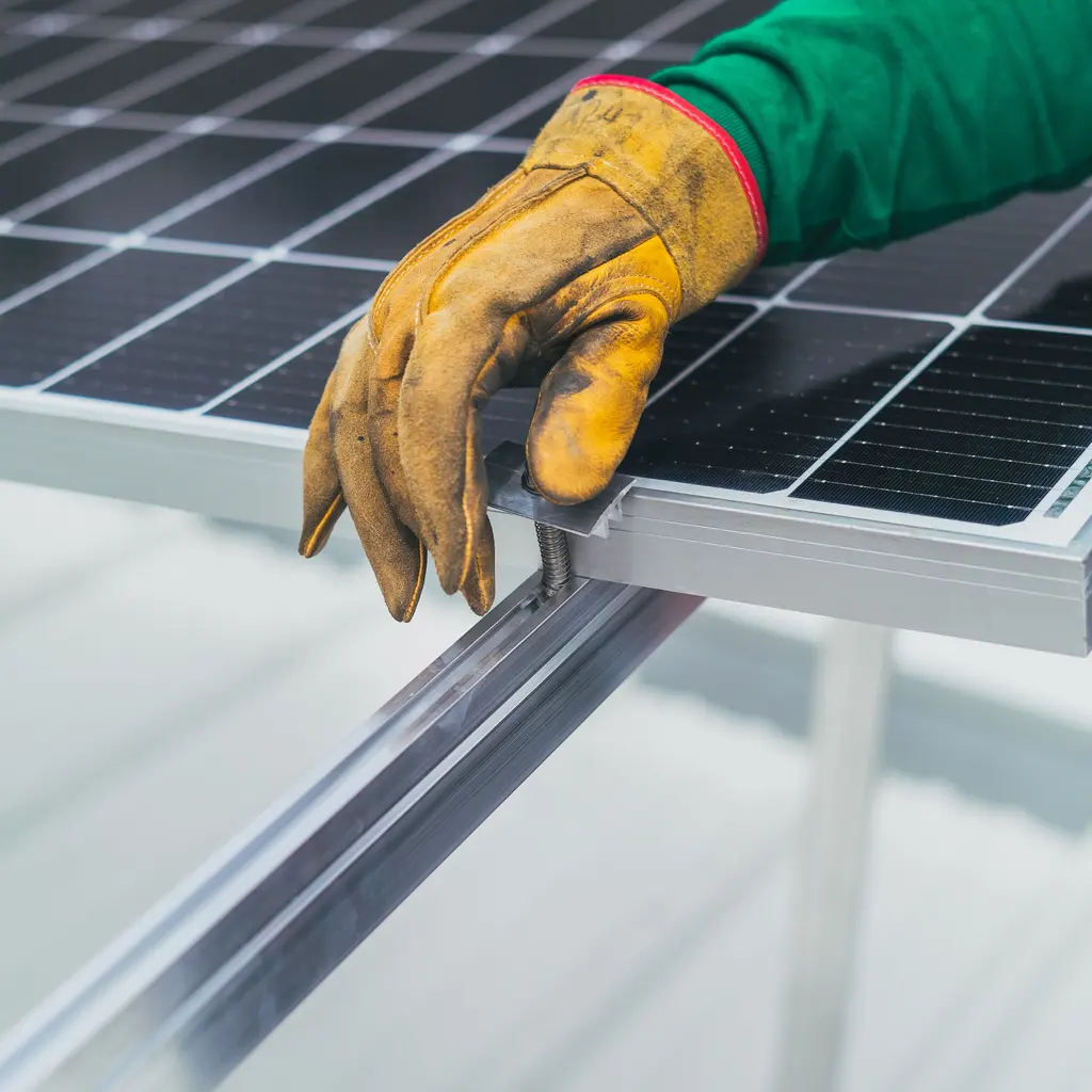 A gloved hand at a solar panel's mounting clamp and support rail.