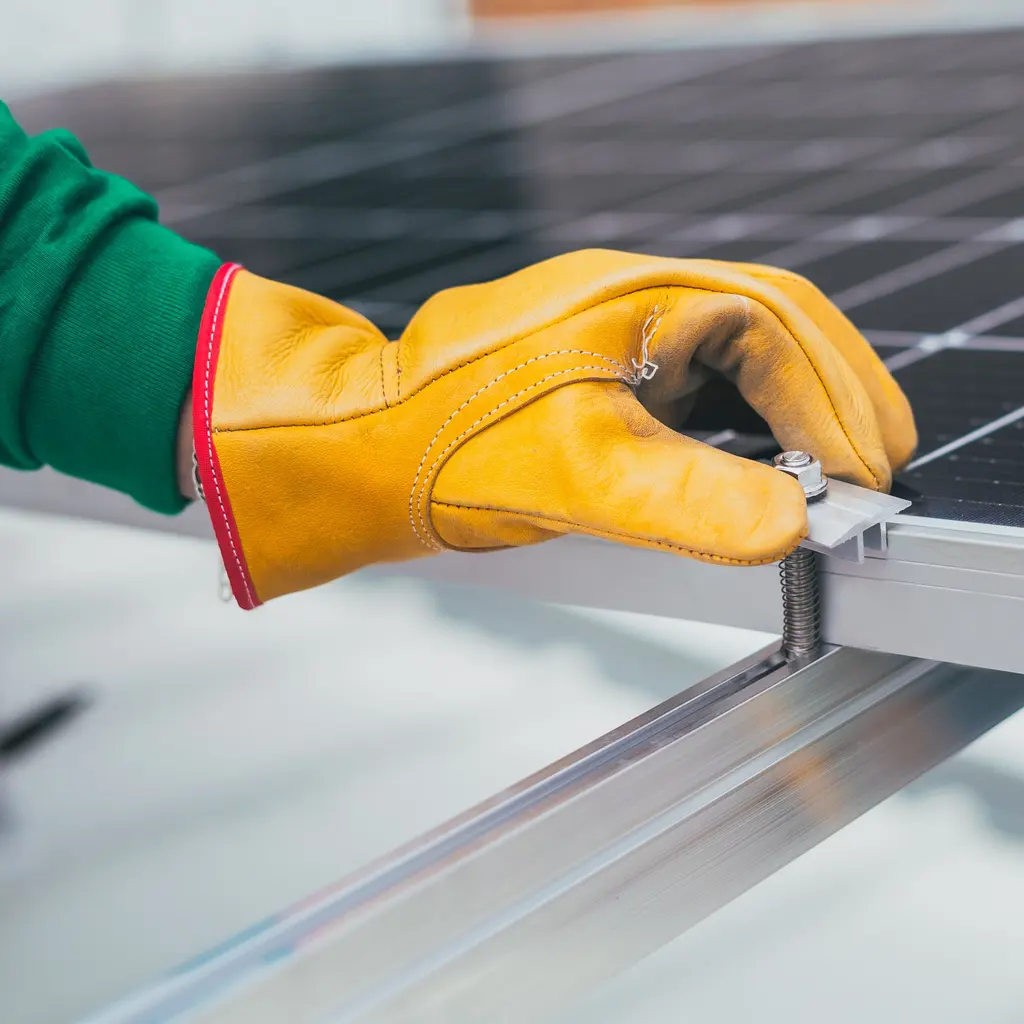 A gloved hand positions a clamp on a solar panel mounting rail.