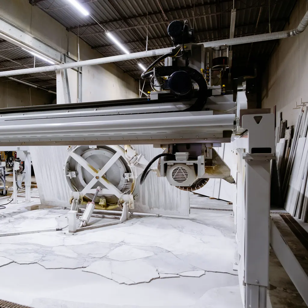 A bridge saw spans a stone-cutting table in a slab fabrication shop.