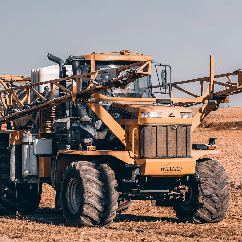A self-propelled agricultural boom sprayer parked on bare ground.