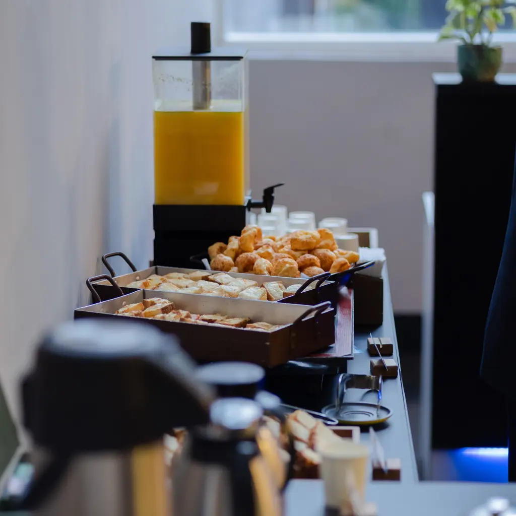 Pastries, serving trays and a juice dispenser arranged for a breakfast buffet.
