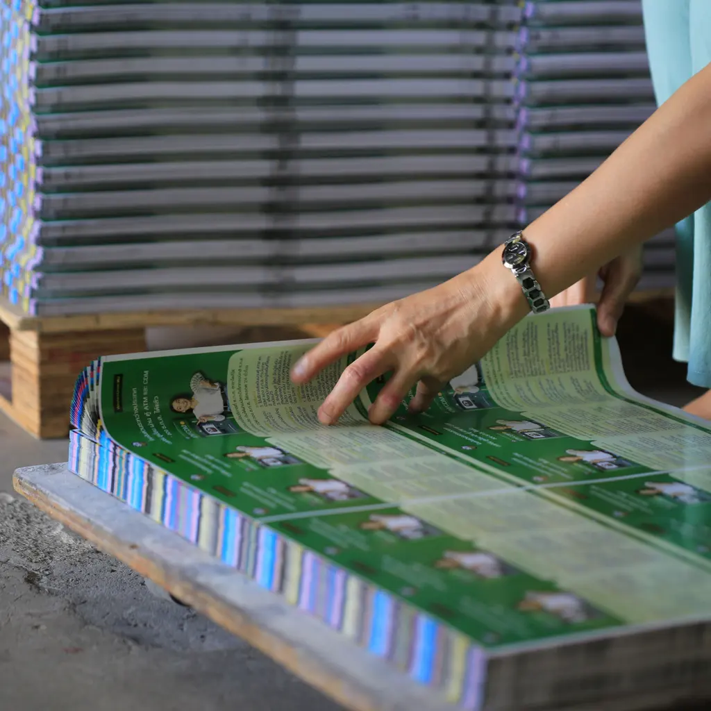 A print worker checking a stack of freshly printed publication sheets.