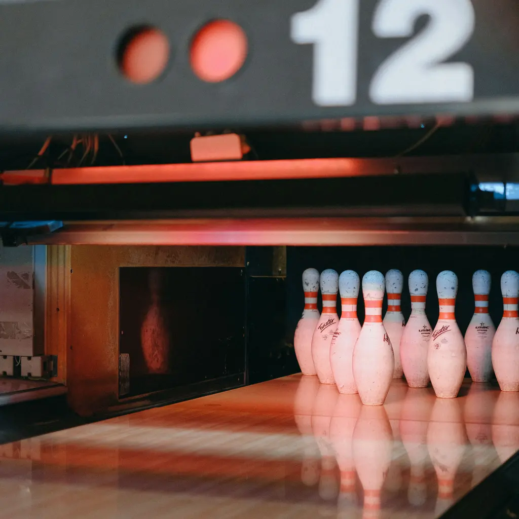 Bowling pins standing at the end of a polished lane beneath a lane-number display.