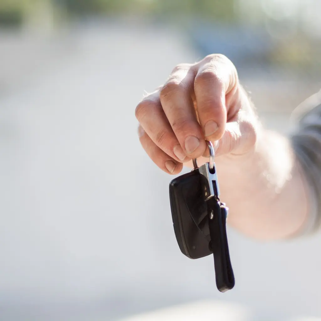 A hand offering a car key and remote fob.