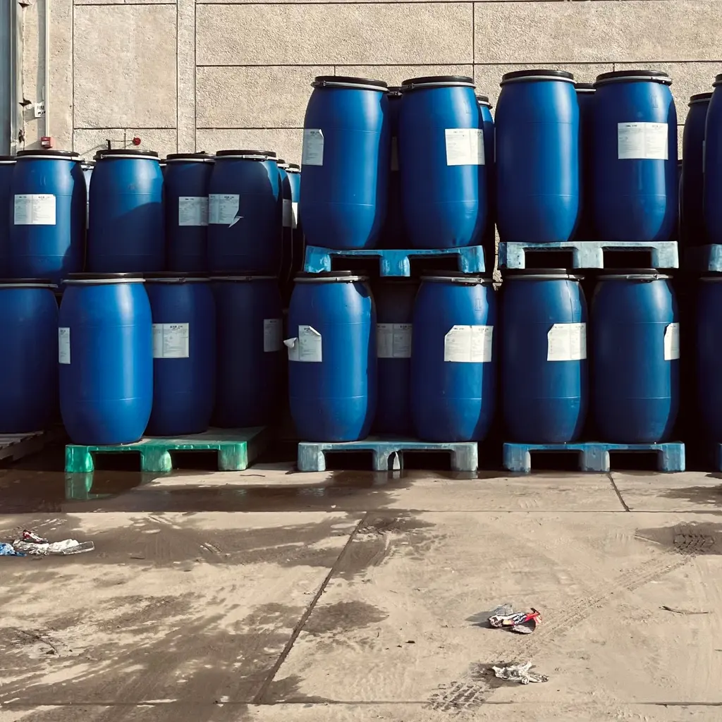 Sealed blue industrial drums stacked on pallets outside a warehouse.