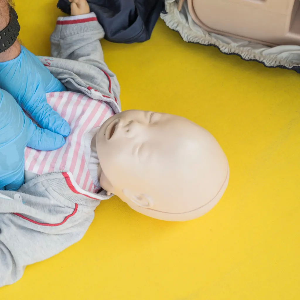 Gloved hands practising with an infant resuscitation training manikin.