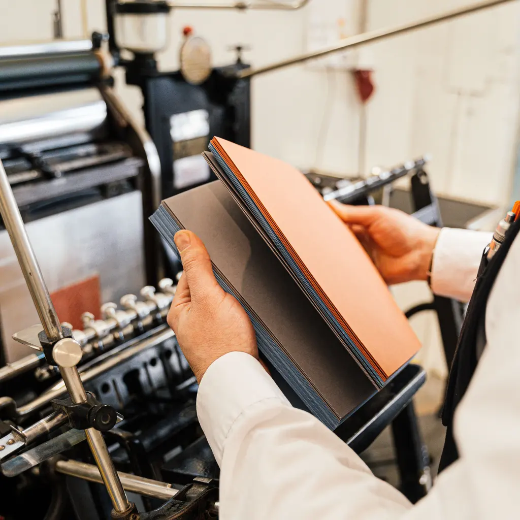 Hands holding a platen component beside a workshop printing press.