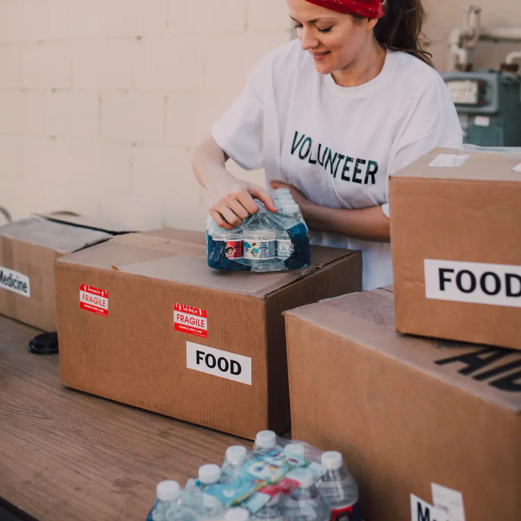 A volunteer packing bottled water beside boxes marked for food distribution.