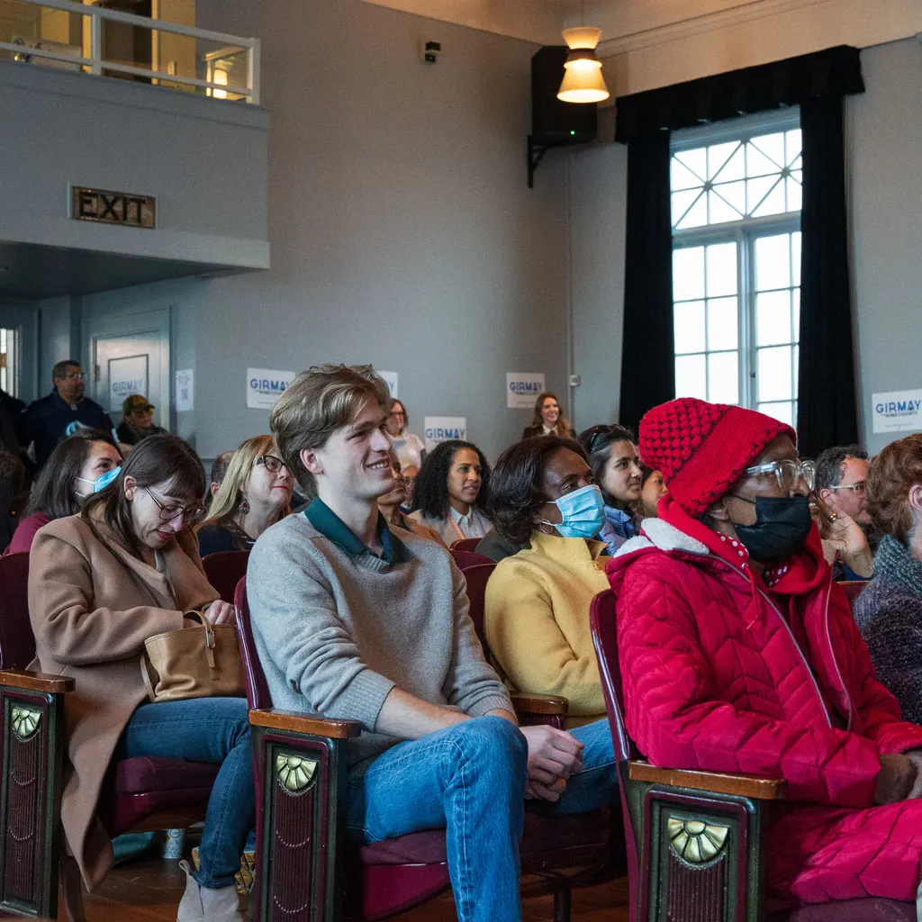 People seated in rows of chairs listening during a community meeting.