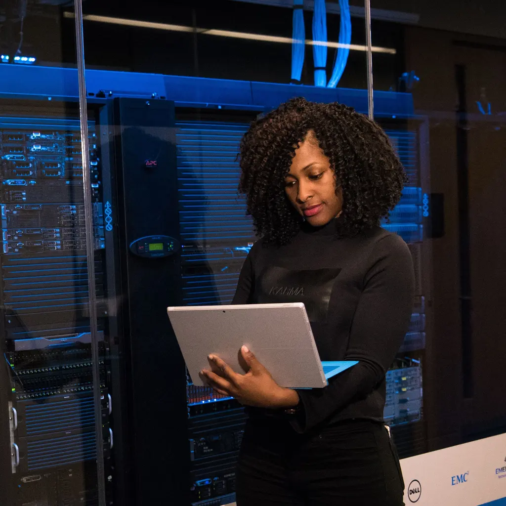 A professional using a laptop beside rack-mounted computer equipment.