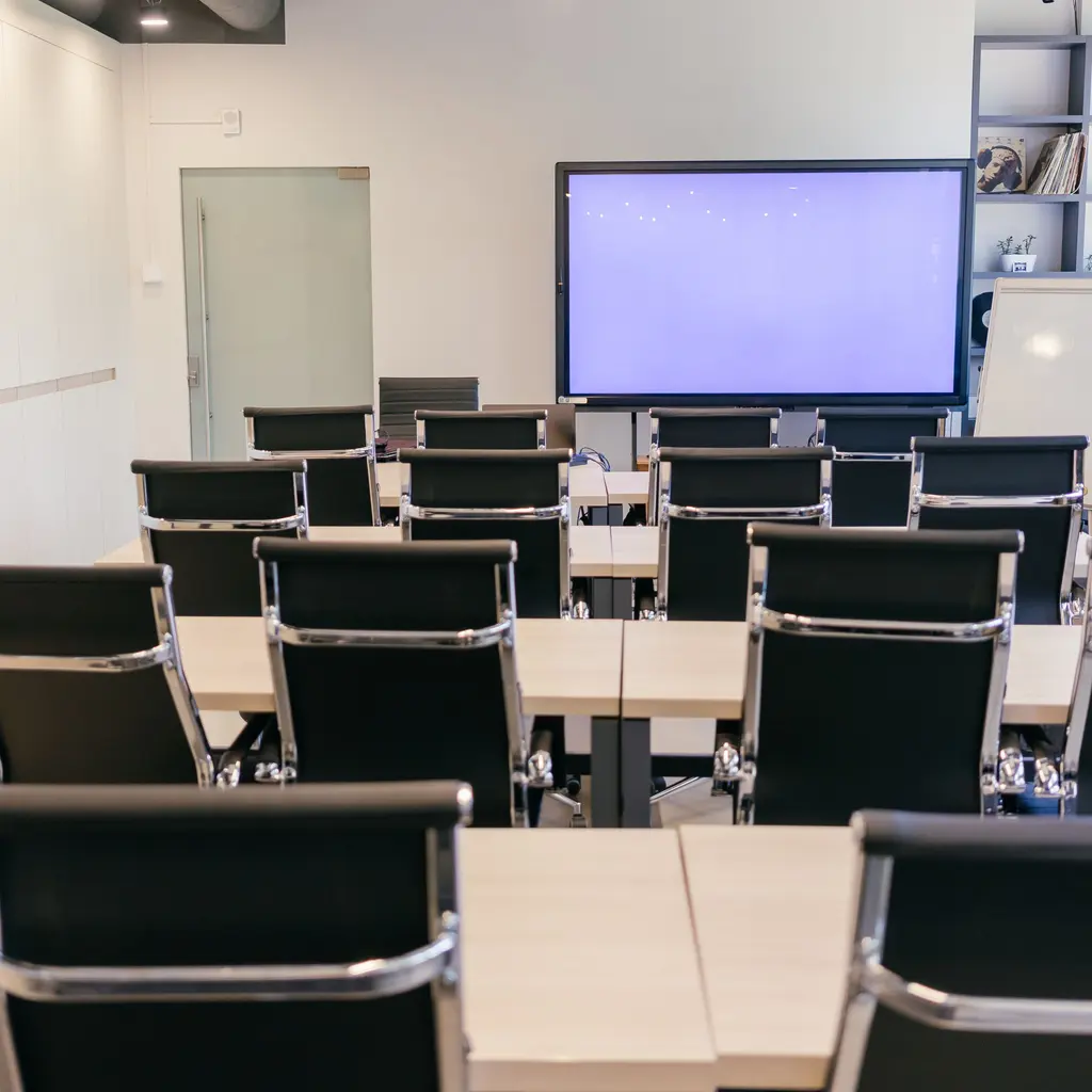 Rows of black chairs and meeting tables facing a presentation screen in a conference room.