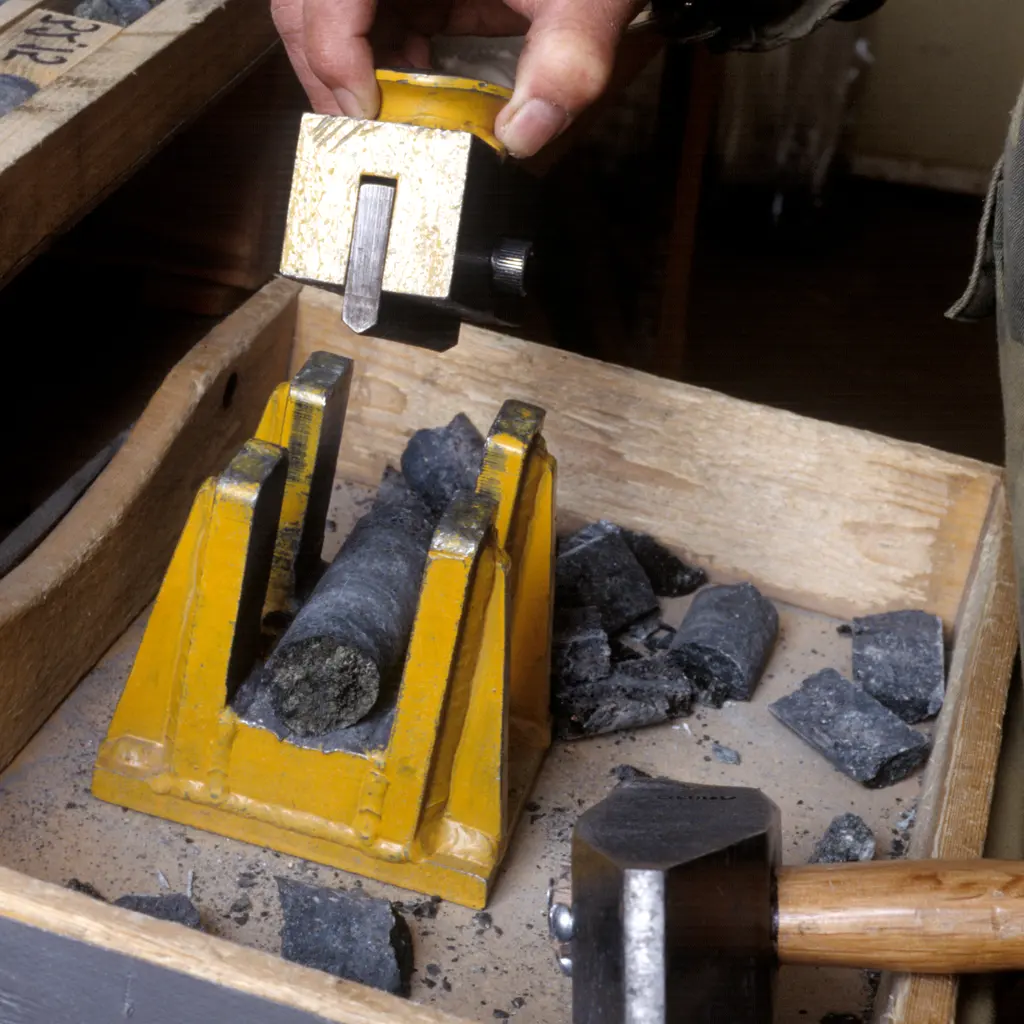 A rock core positioned in a splitting tool beside a hammer and sample trays.