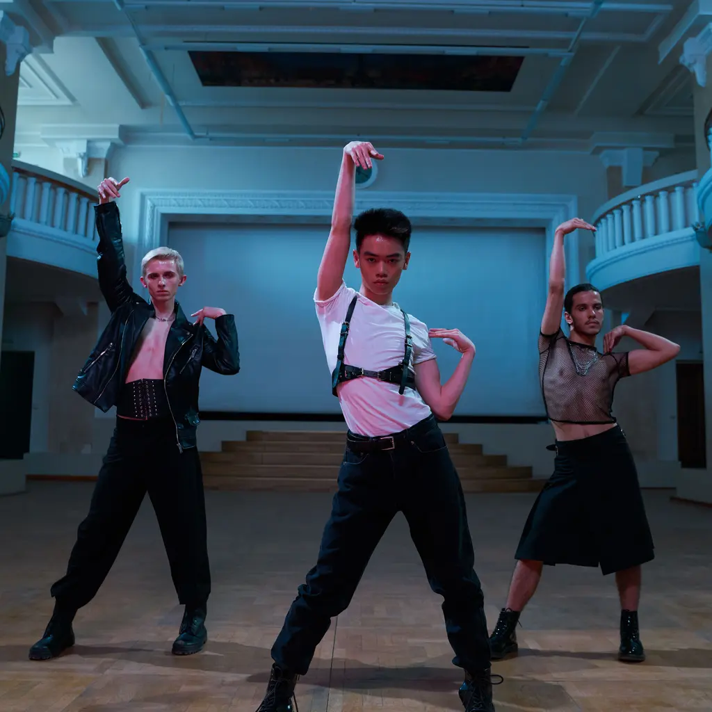 A group of adult dancers rehearsing coordinated movements in a studio.