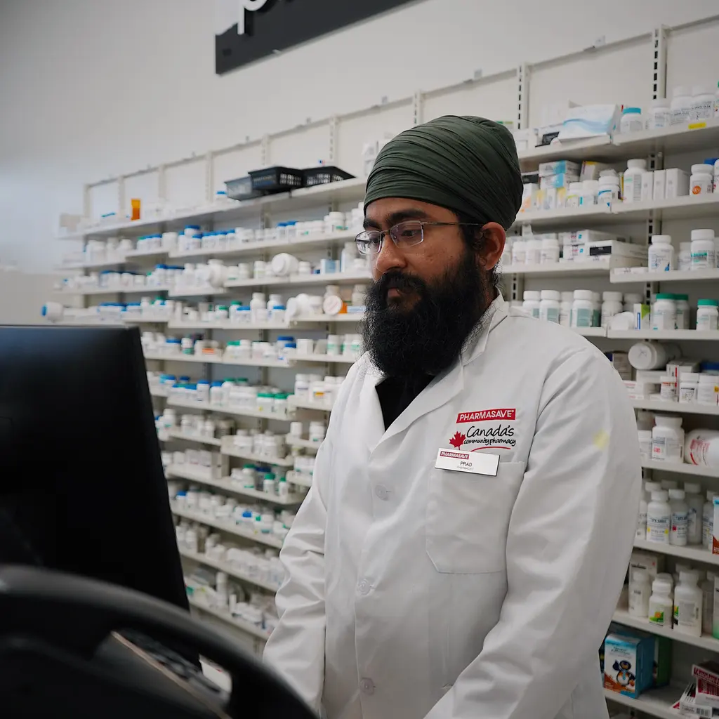 A pharmacist working at a computer in front of shelves of medicine.