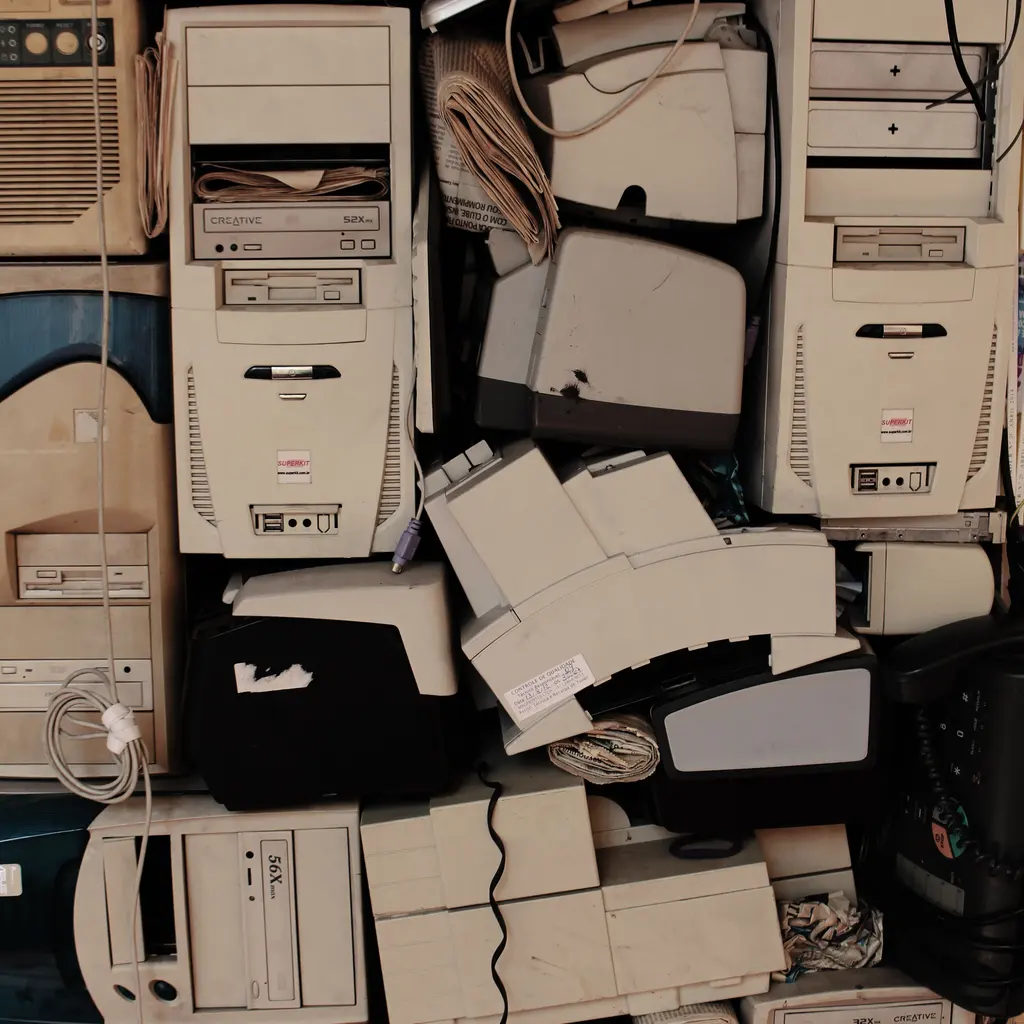 Old computer cases, printers and loose cables stacked together.