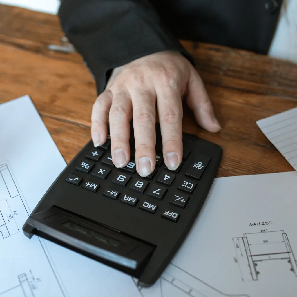 A hand using a calculator beside technical drawings and written calculations.