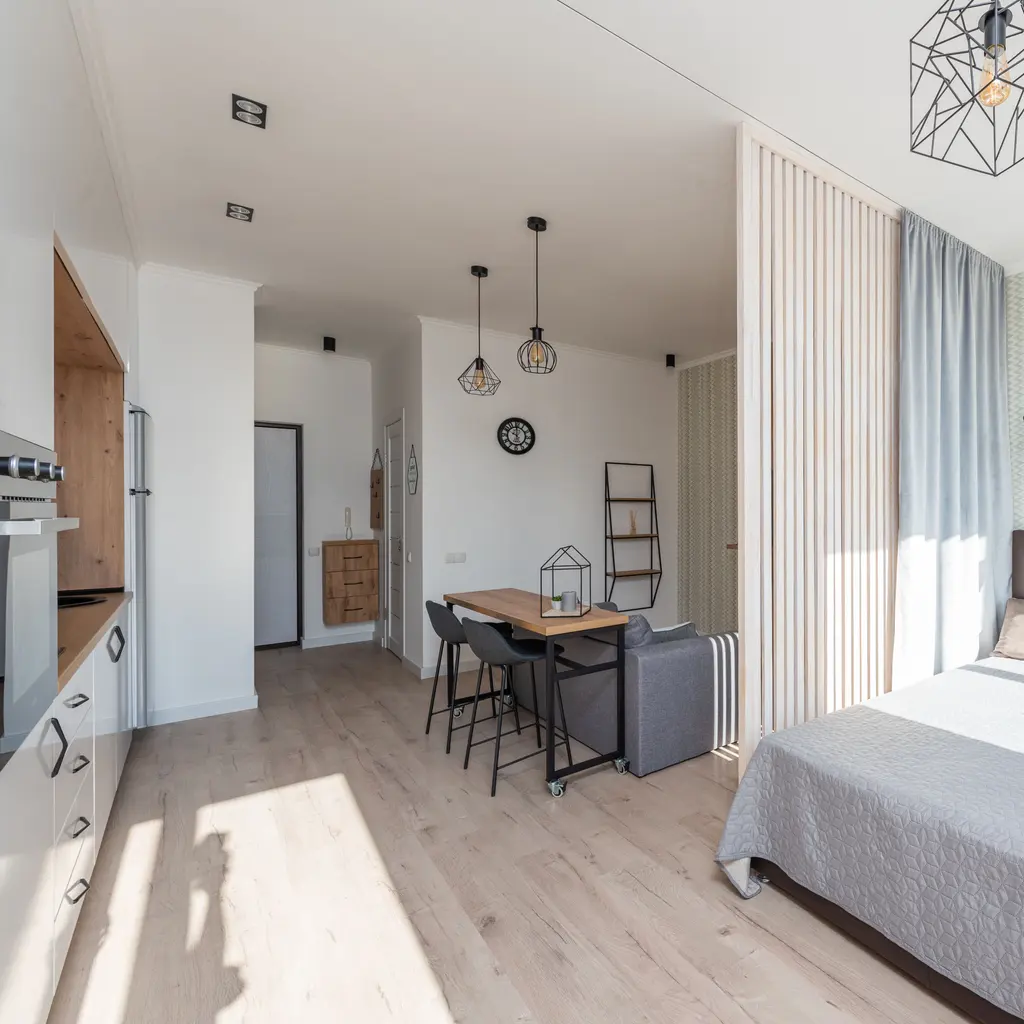 A compact furnished suite with cooking appliances, a dining table and a bed.