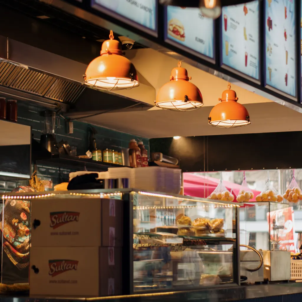 Menu screens and warm pendant lights above a quick-service food counter.