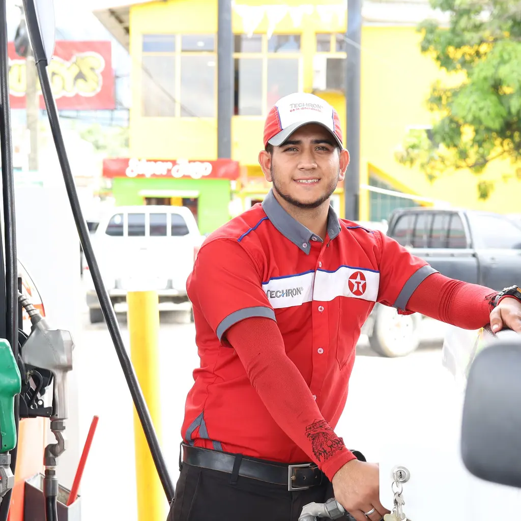 A uniformed fuel-station attendant beside a vehicle and dispensers.