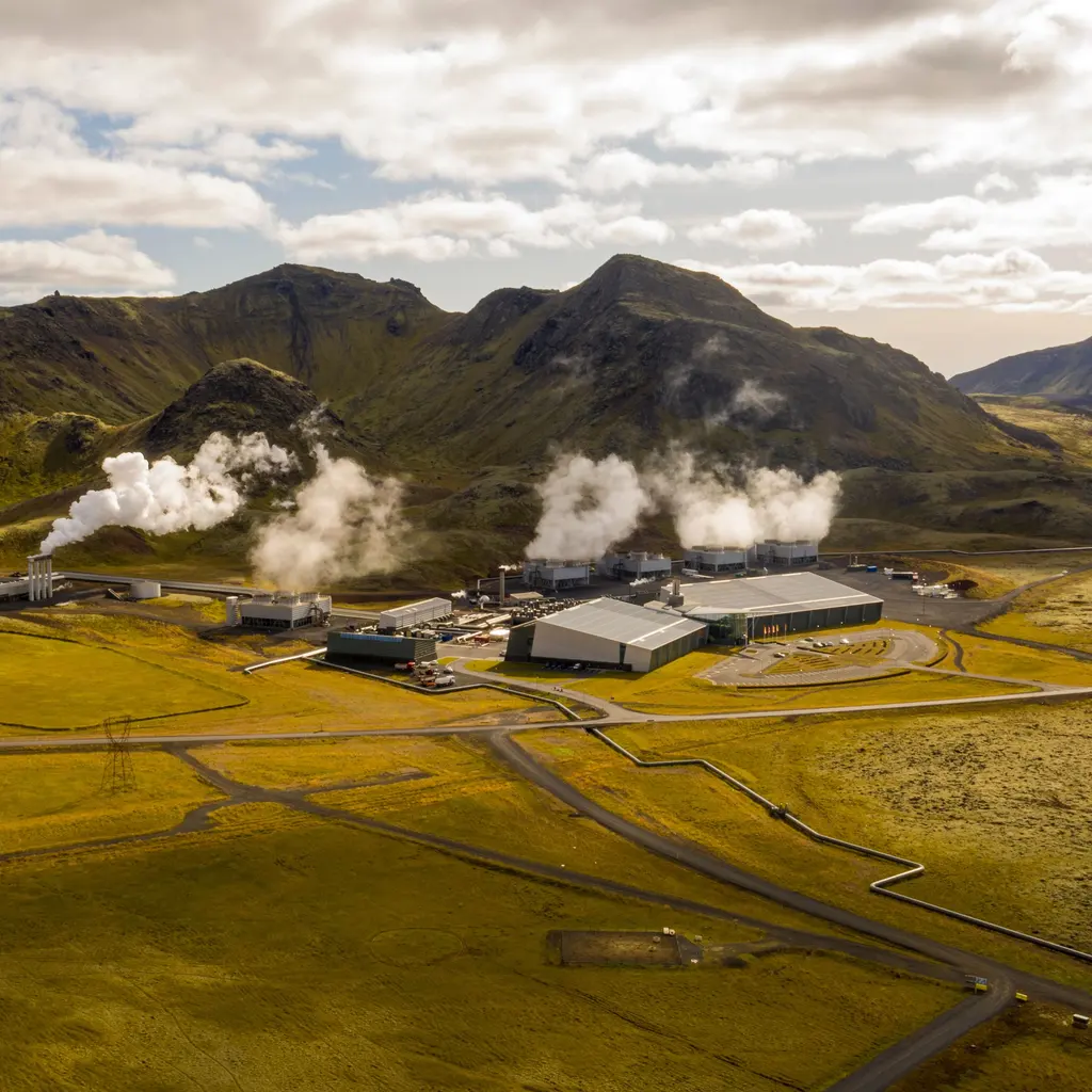 A geothermal power complex with steam plumes and pipework across the surrounding terrain.