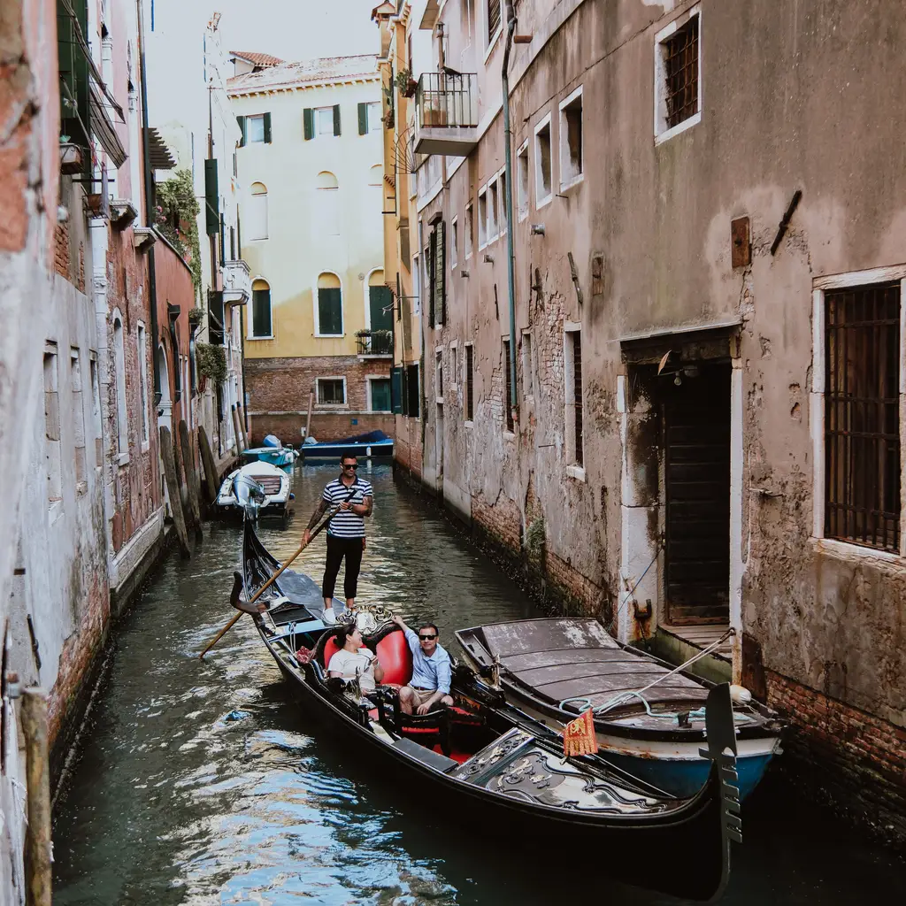 A gondolier steering passengers through a narrow canal.