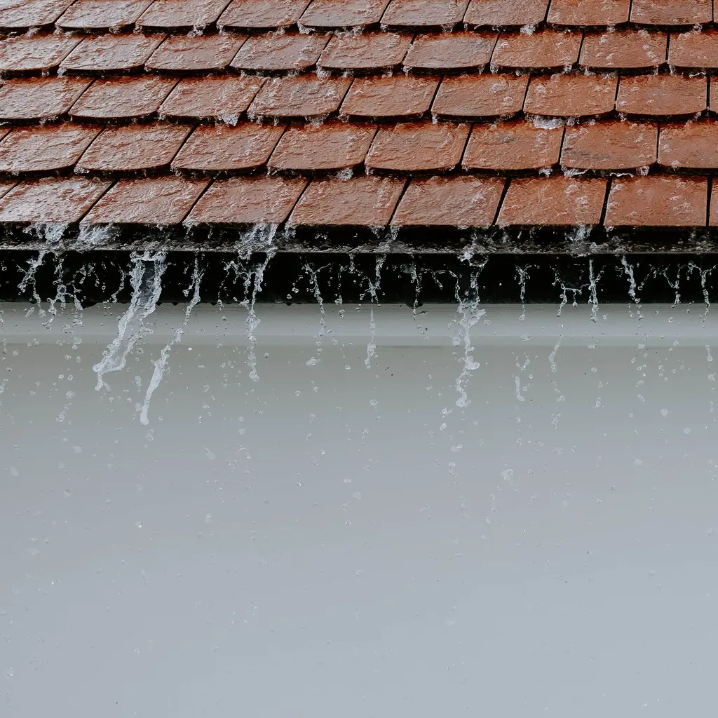 Rainwater spilling over a dark gutter below a tiled roof.
