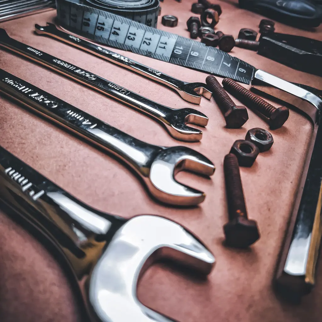 Metal wrenches, bolts, nuts and a measuring tape arranged on a work surface.