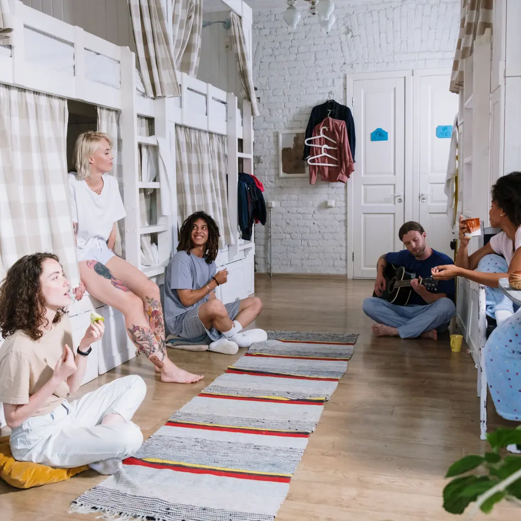 A group sitting together between curtained bunk beds in a shared dormitory.