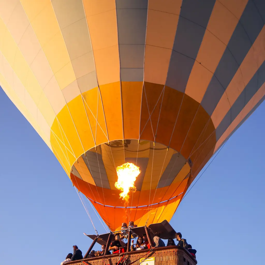 A hot-air balloon's burner firing above a suspended passenger basket.