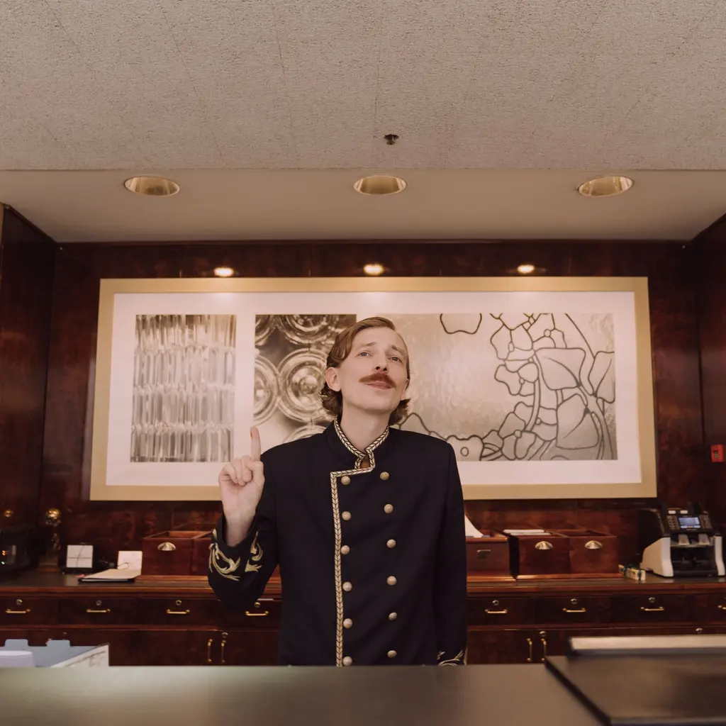 A uniformed receptionist standing behind a polished wooden hotel front desk.