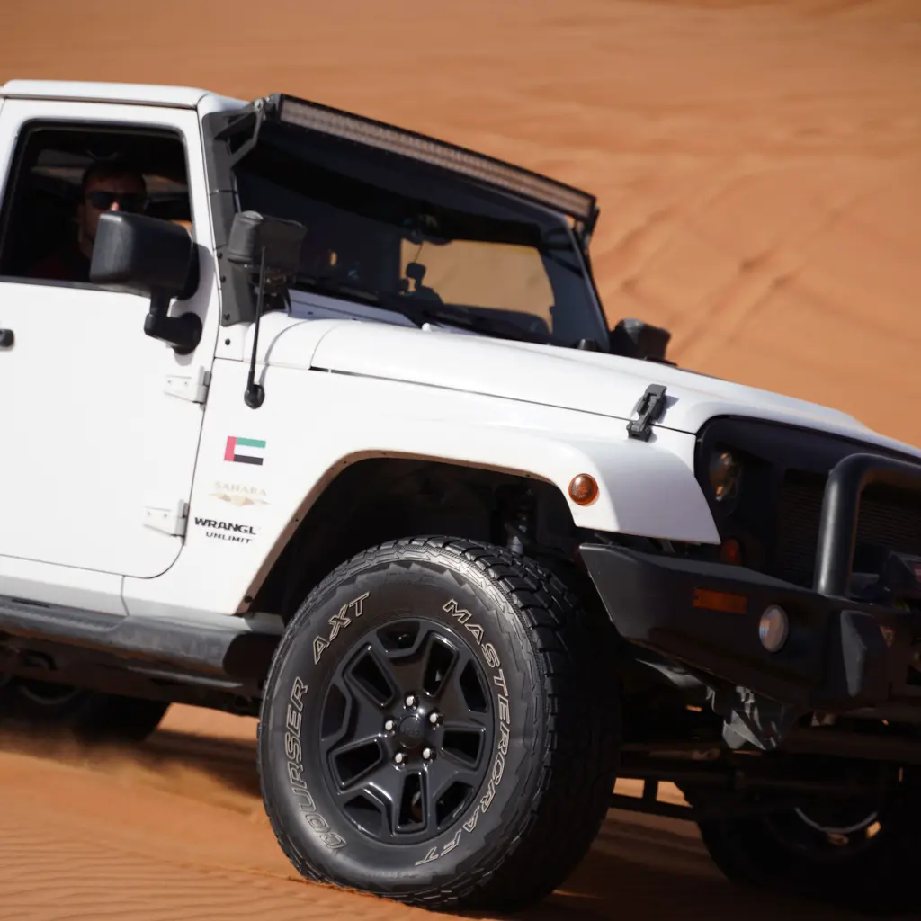A white off-road vehicle crossing orange sand dunes.