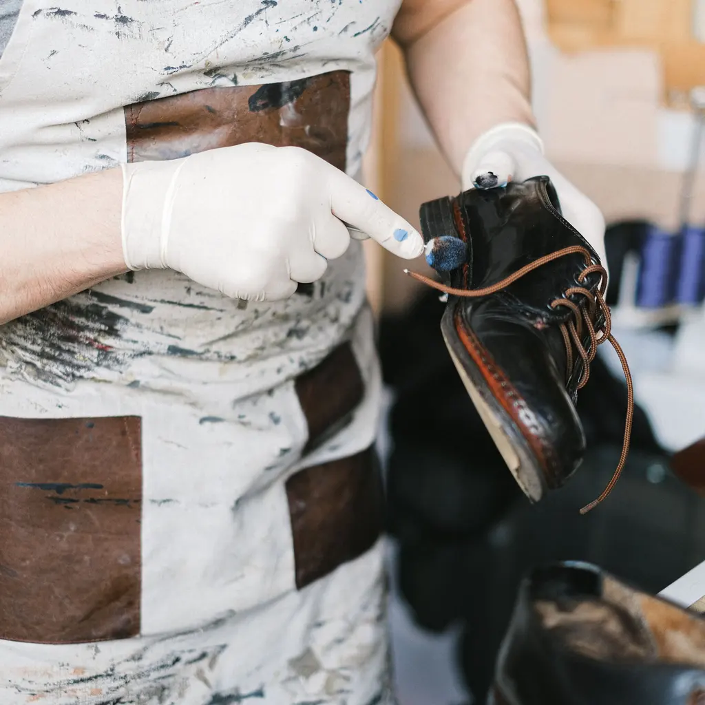 Gloved hands treating the finish of a black leather shoe.