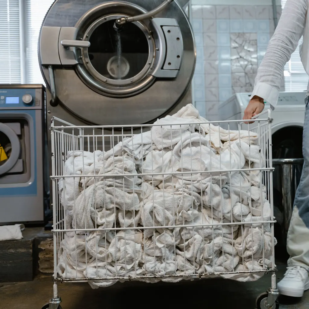 A cart full of white linens beside an open commercial washing machine.
