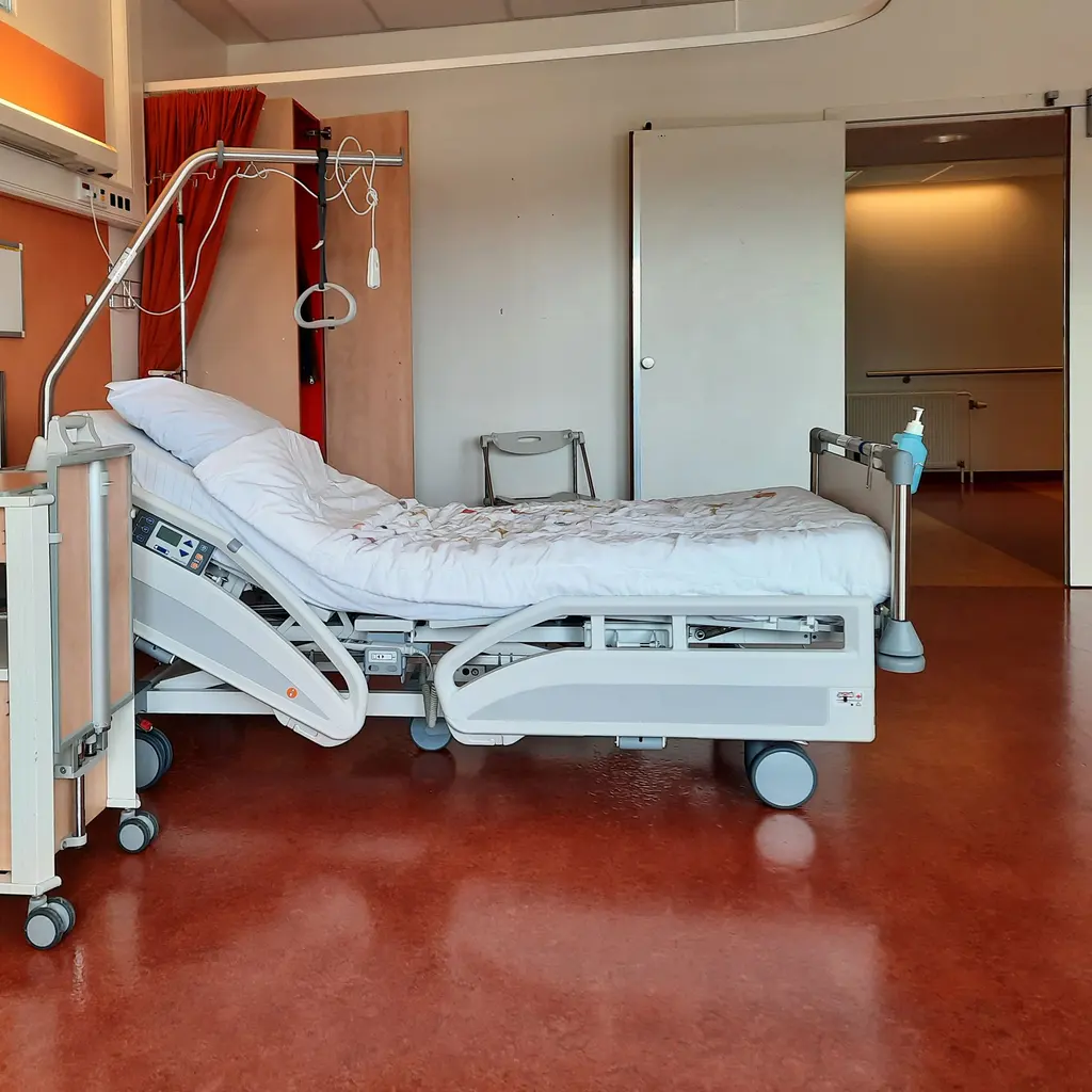 An unoccupied adjustable care bed with an overhead assistance handle.
