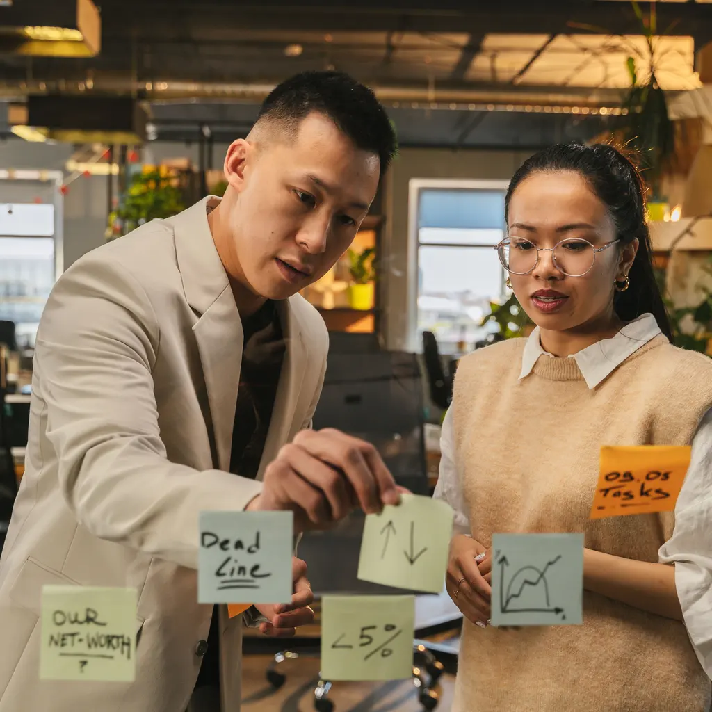 Two people reviewing planning notes and charts on a glass board.