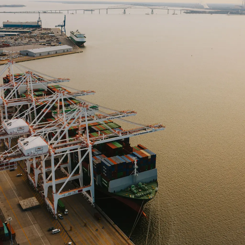 Container cranes extending over a cargo ship at a port berth.