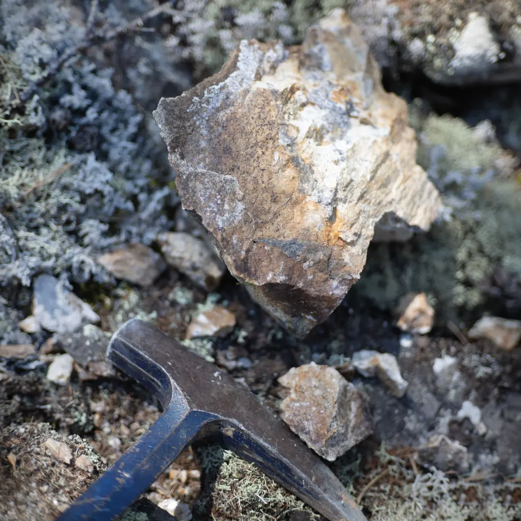 A geological rock hammer beside broken rock and mineral fragments.