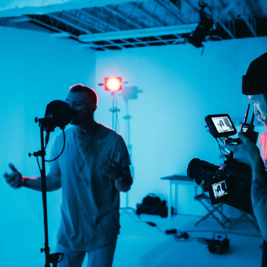 A camera operator filming a vocalist at a microphone in a studio.