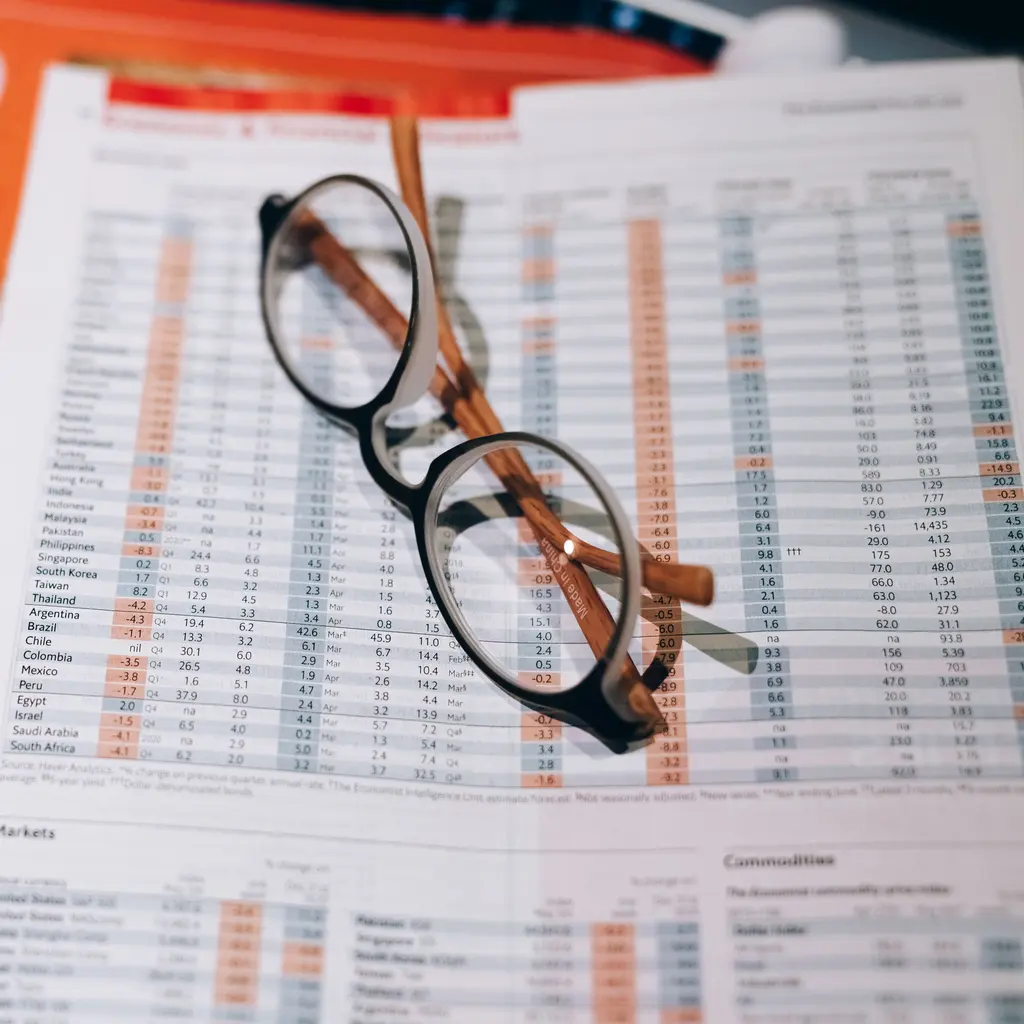 Printed financial-market price tables beside reading glasses.