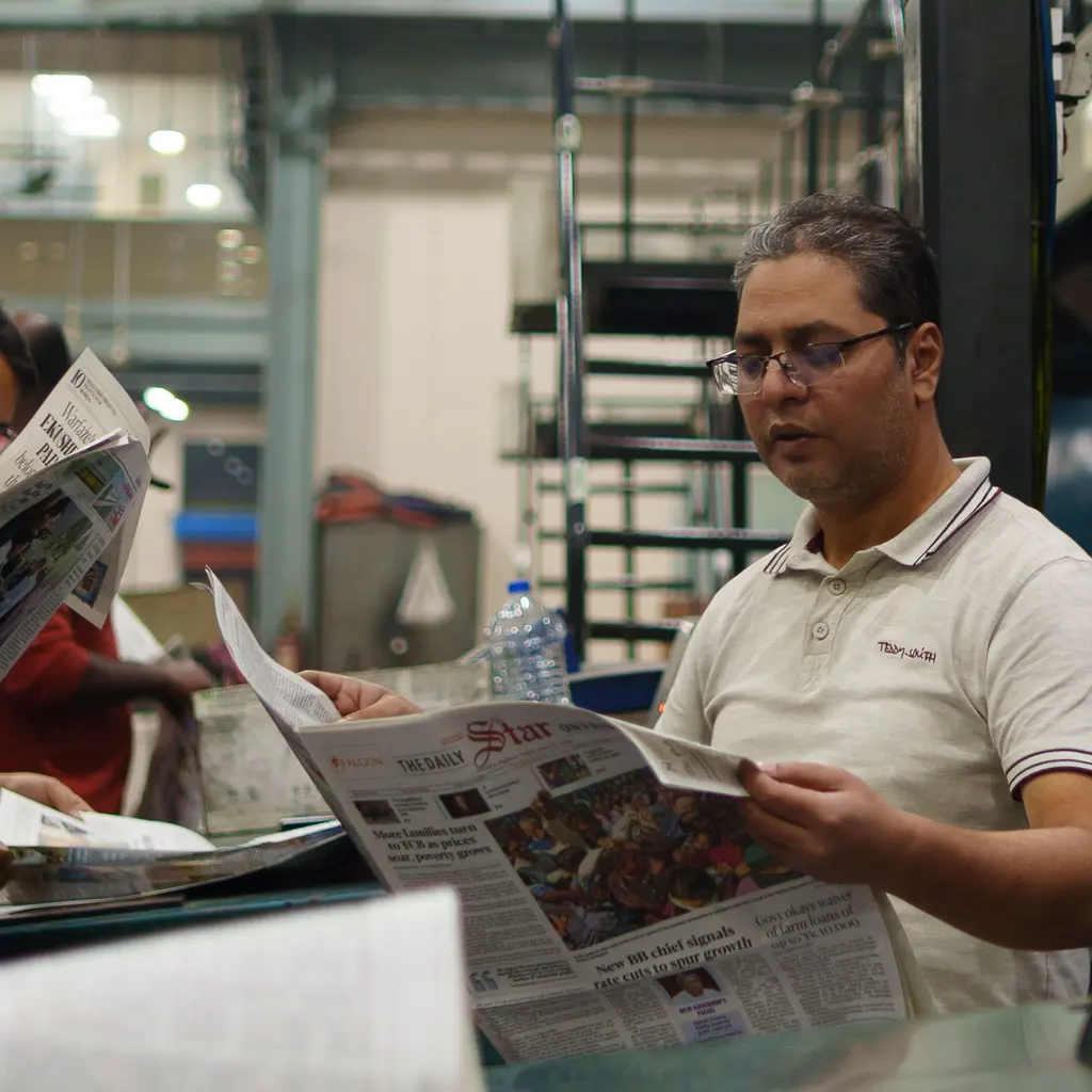 Print-room workers checking freshly printed newspapers beside the press.