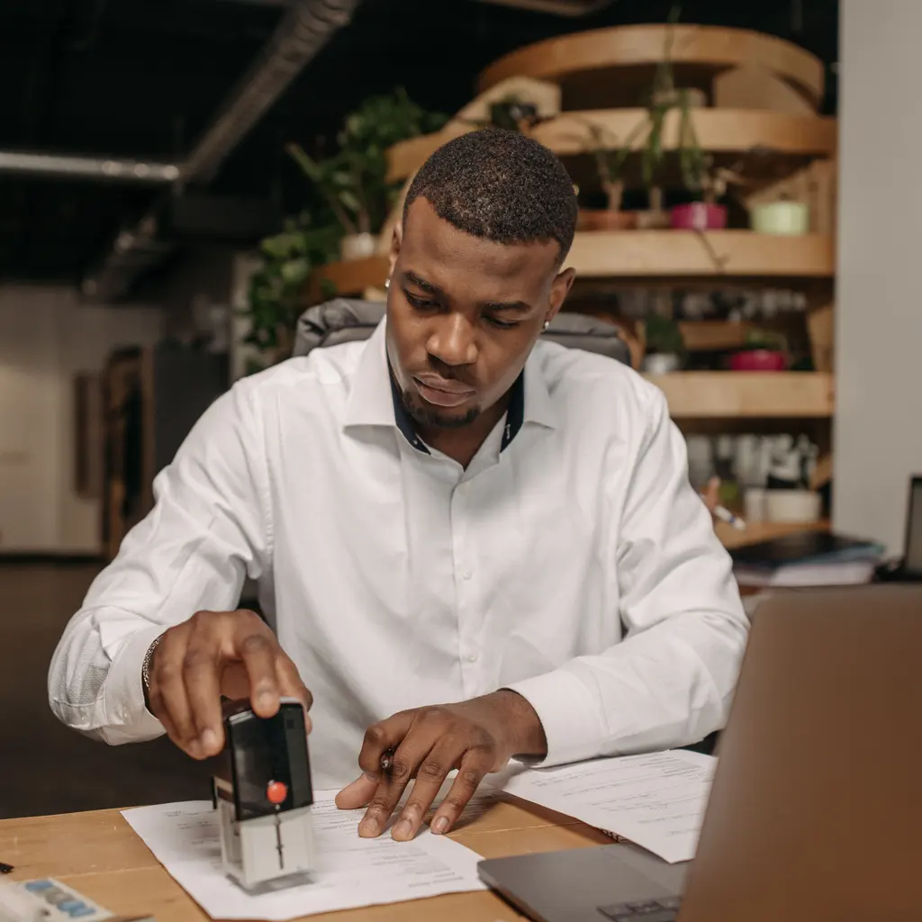 A person applying a self-inking stamp to a document at a desk.