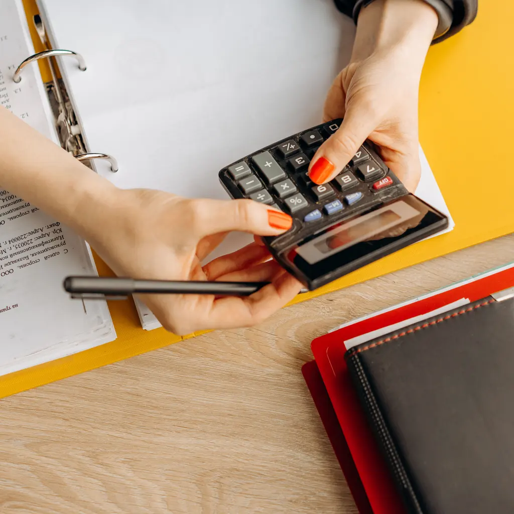 Hands using a calculator beside an open binder and folders.