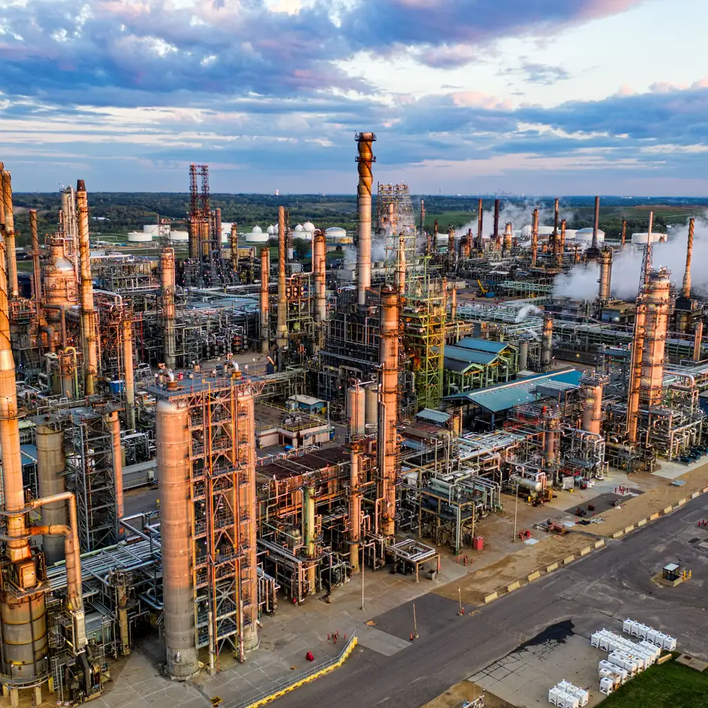 An aerial view of an oil refinery's processing towers and interconnected pipework.