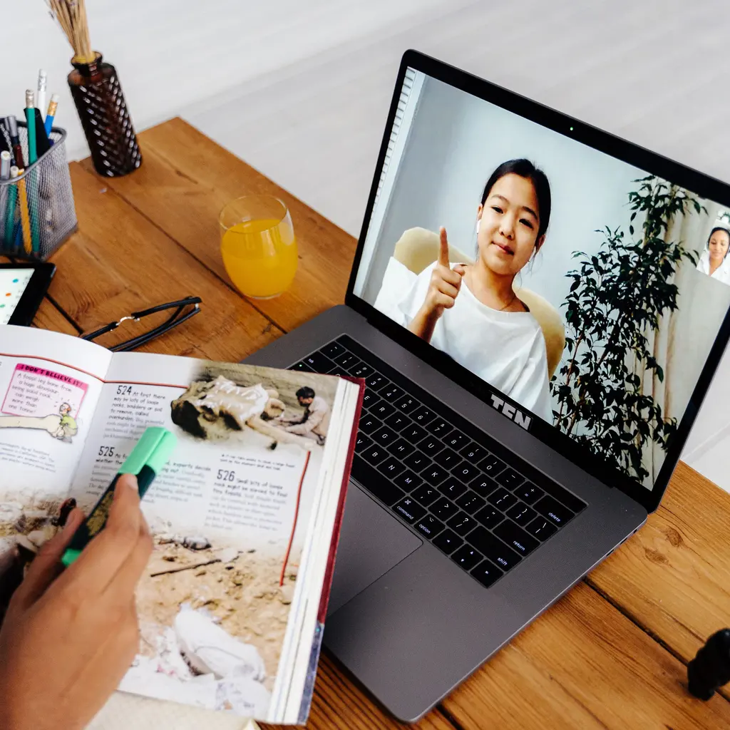 An online lesson on a laptop beside an open study book.