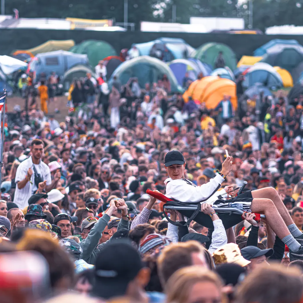 An outdoor music-festival crowd with a camping area behind it.