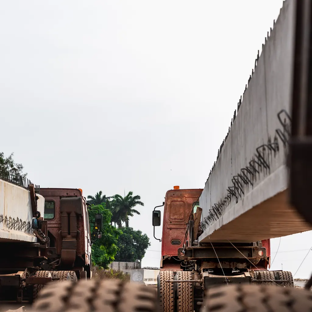 Long precast concrete beams carried on multi-axle transport trailers.