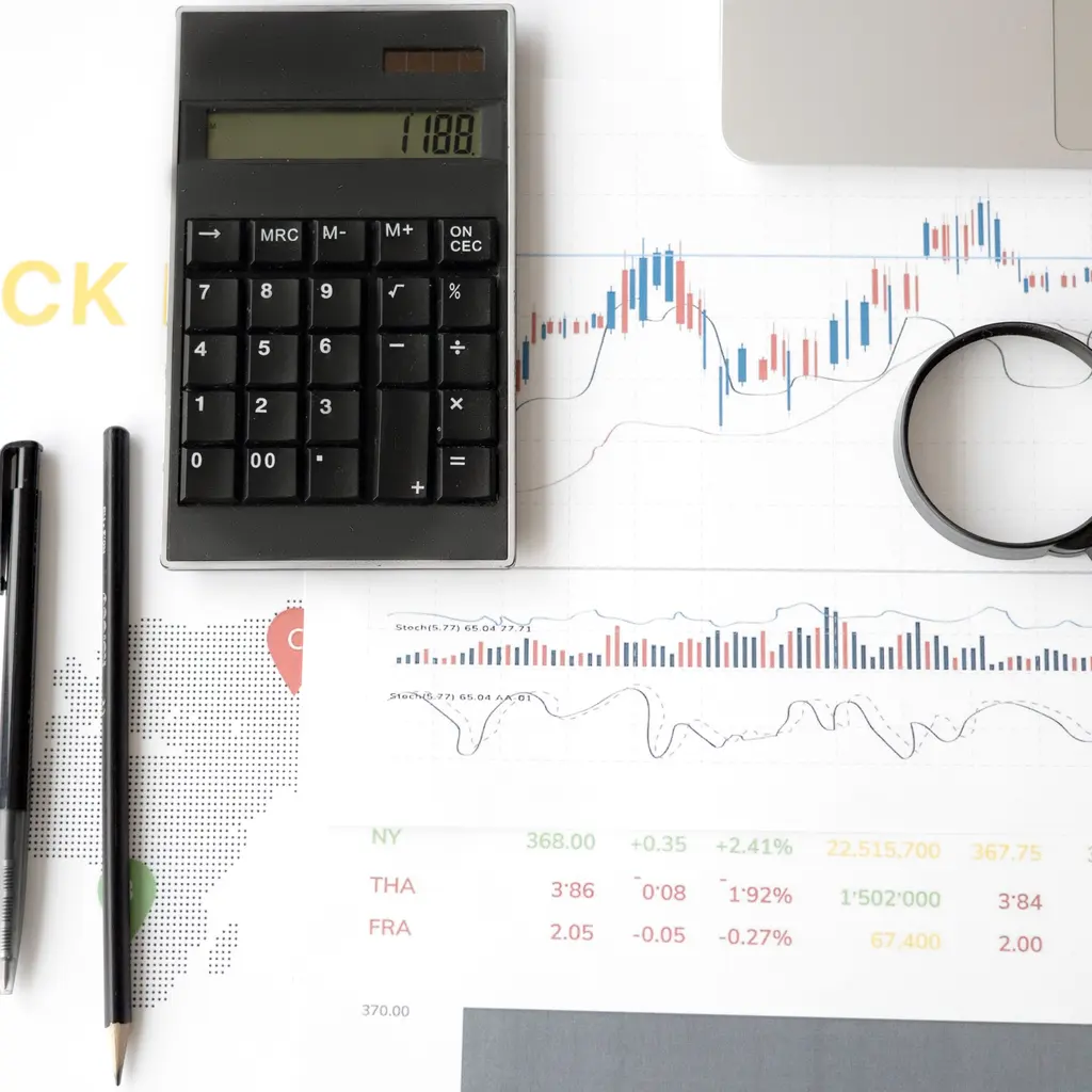 A calculator and magnifying glass beside printed stock-market charts.