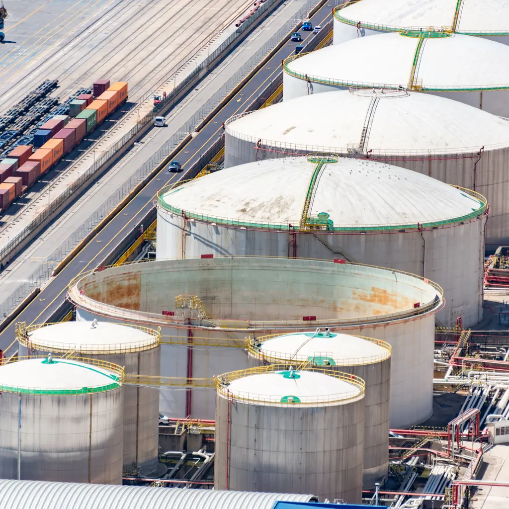 Large liquid-storage tanks and pipework beside railway sidings.